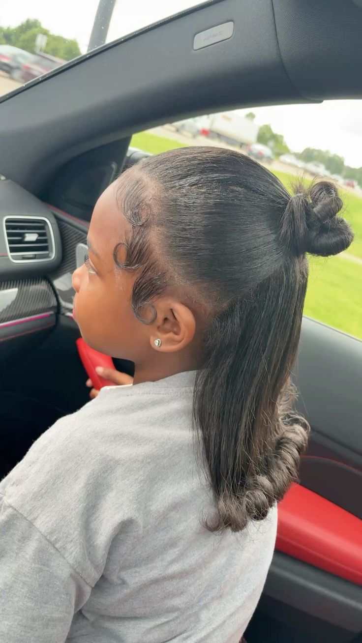 A young black girl in a car with a well styled  half up bun and cute baby face for the edges