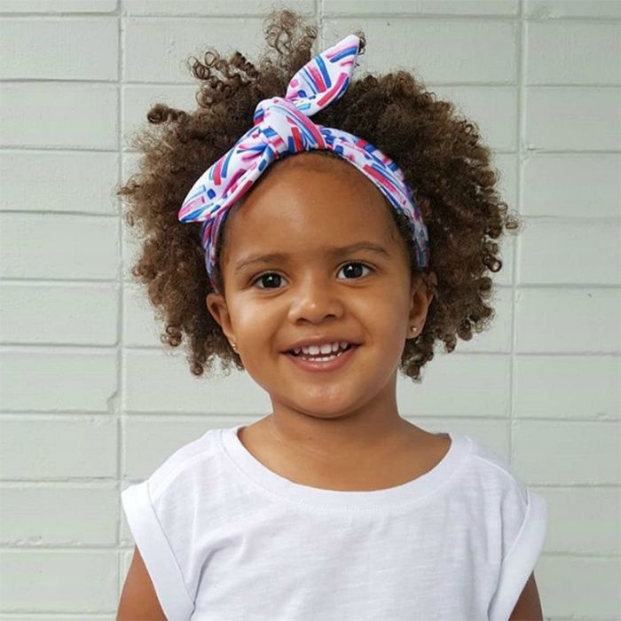 A cute little girl in a white background smiling while look at the camera with her cute simple head band hair style