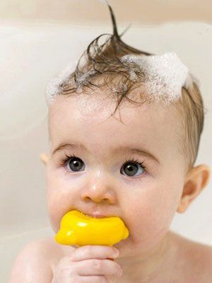 A baby with wet, foam-covered hair during bath time, holding a yellow rubber duck toy, illustrating a gentle wash day moment for baby hair."