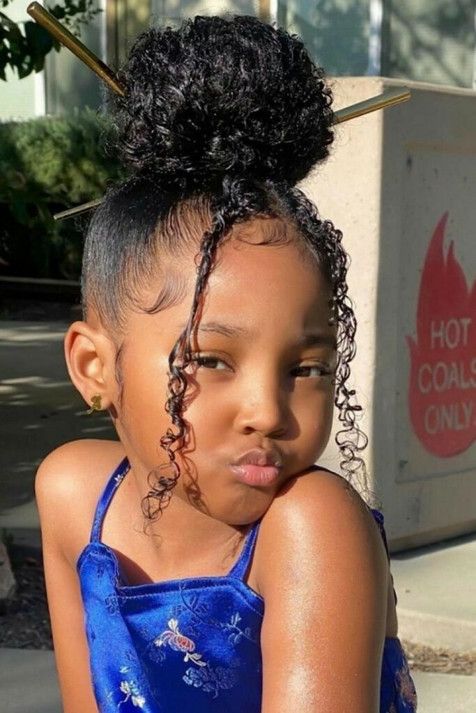 Cute kids hairstyle with a sleek curly high bun and soft face-framing curls