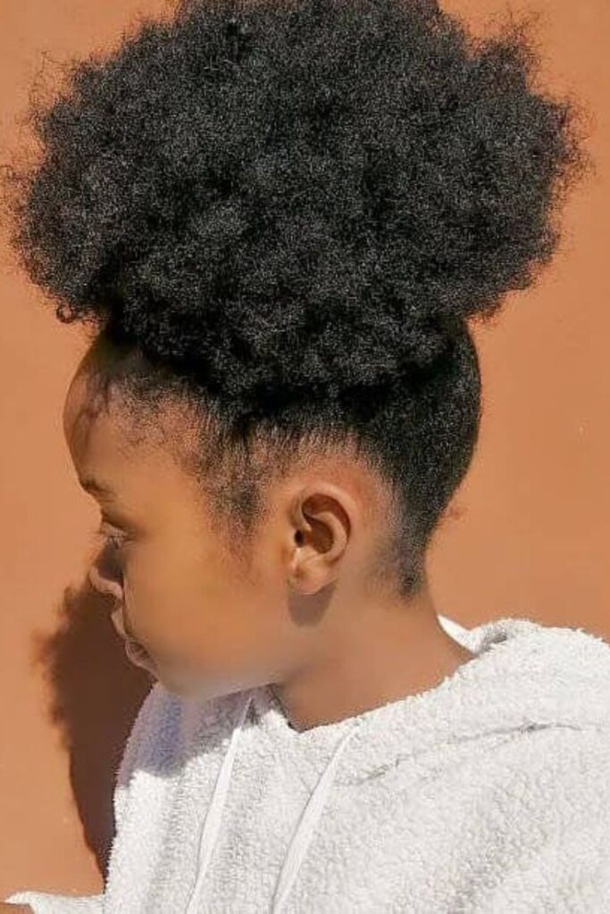 Child with natural curls styled into a high puff for volume and easy styling