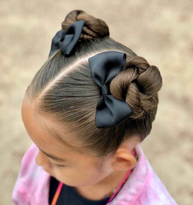 Child wearing two symmetrical space buns, one on each side of the head with a bow on each bun
