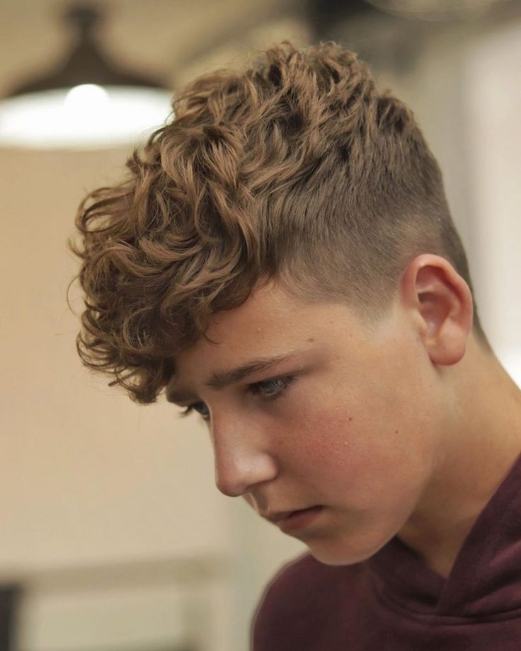Side profile of a boy with textured curly fringe on top and a faded, tapered side, styled as a curly crop.