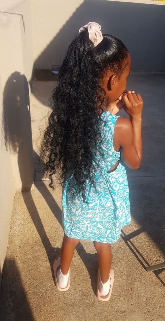 Young girl with a high curly ponytail secured with a scrunchie, hair falling in long spiral curls