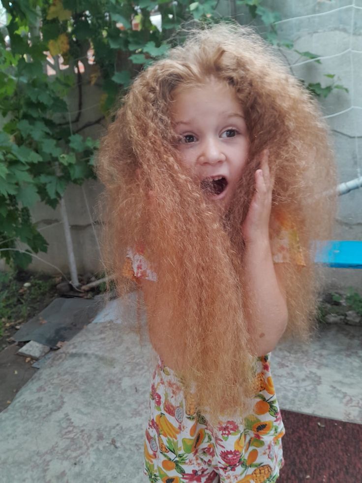 Girl outdoors with extremely frizzy, voluminous curly hair, holding her hair in surprise.