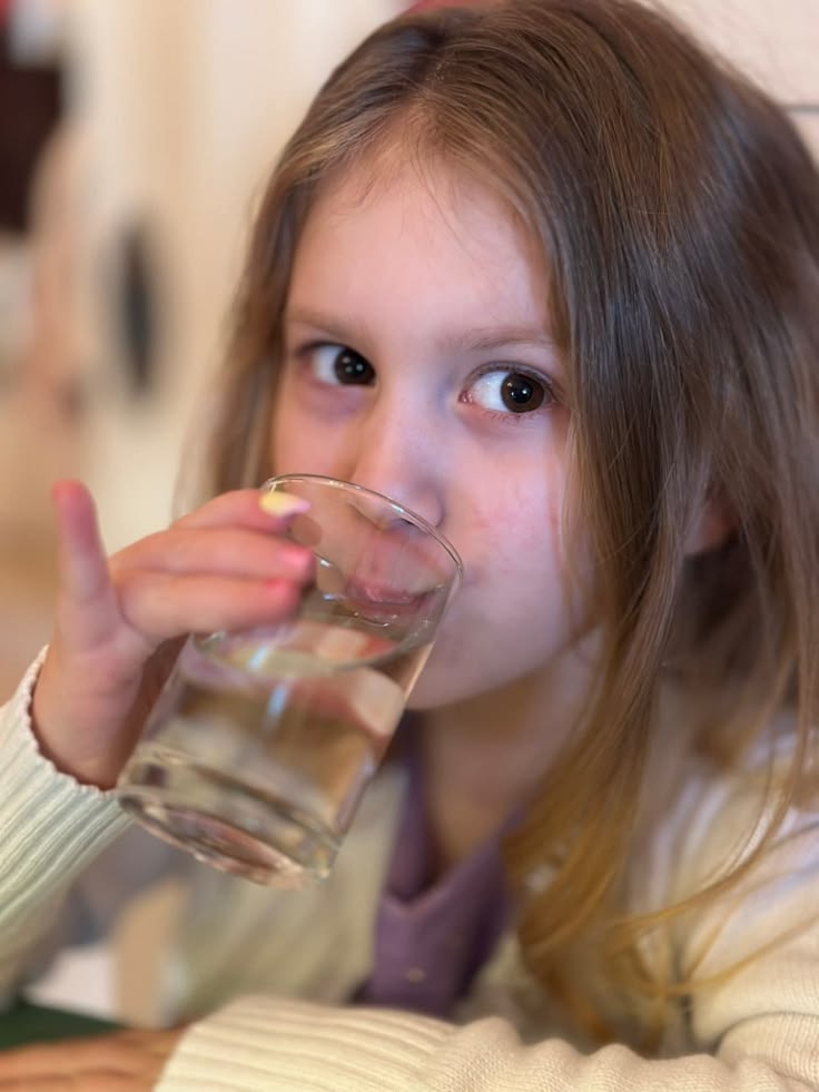 Child drinking a glass of water indoors in spring