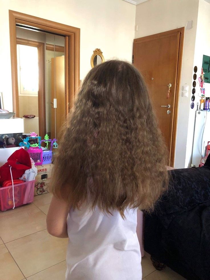 Young girl with long wavy hair showing frizz throughout, shown from behind