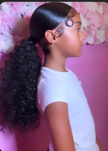 Girl with a curly low ponytail against a floral backdrop.