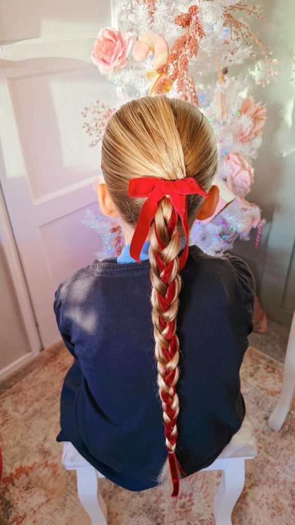 young girl with a red ribbon braided into her ponytail with a red bow attached to it.