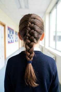 A young white girl in a deep school uniform wearing her hair in a single braid down the back