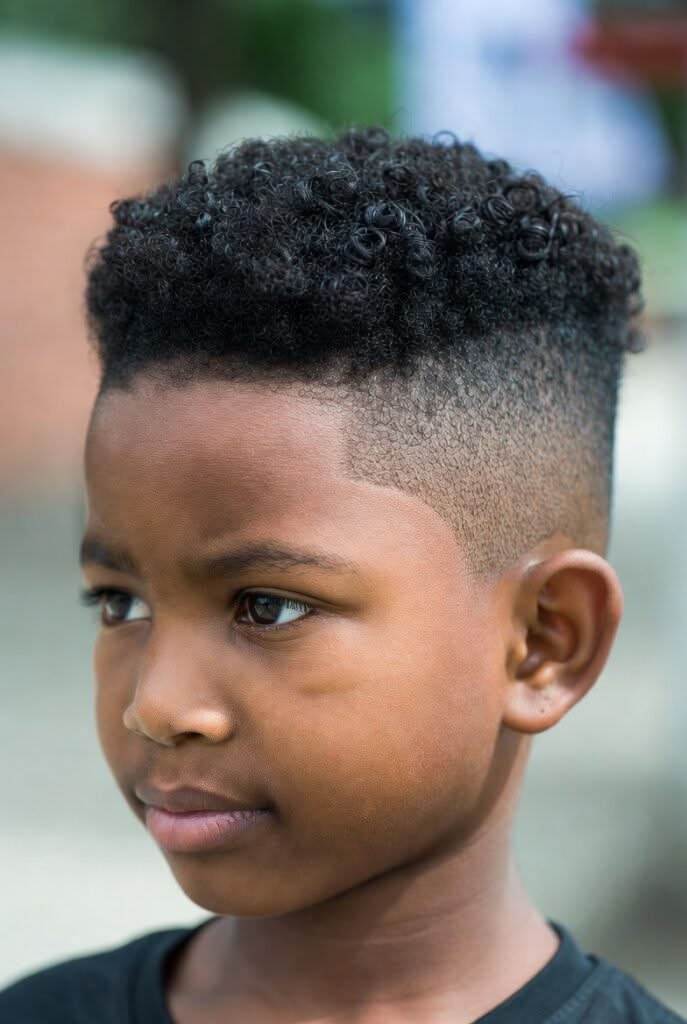 Boy with a high top fade haircut, tall boxy curls on top and sides faded cleanly to skin.