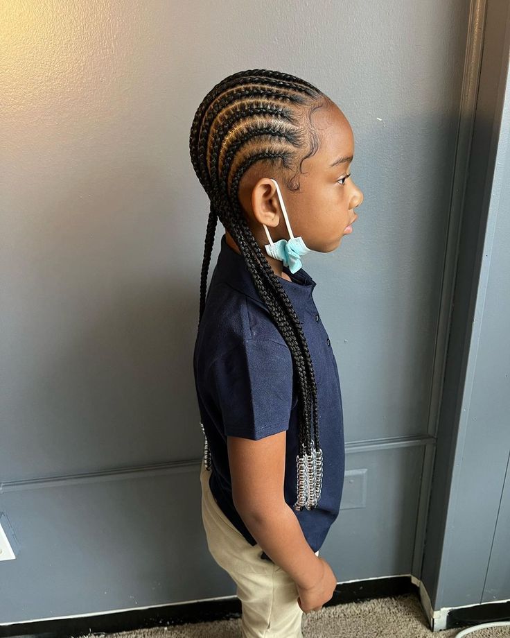 A child wears straight-back cornrows with metal cuffs at the ends, showing a classic long-lasting braided style.