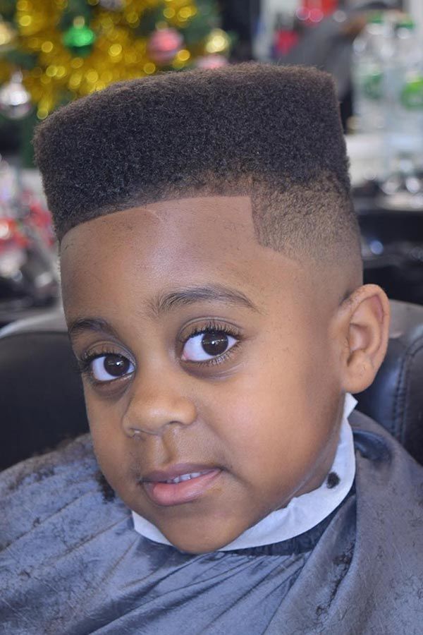 Boy with a flat top haircut, hair squared off level across the crown with faded sides, festive background.