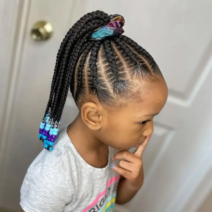 A child wears feed-in braids gathered into a high ponytail with a scrunchie, finished with colorful beads.