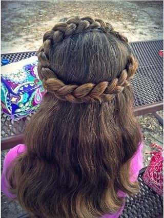A child wears a braided halo across the crown with the rest of her hair left loose and wavy