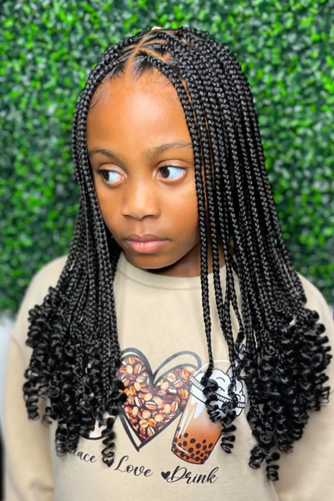 A child wears box braids with a clean middle part, finished with curly extension ends.