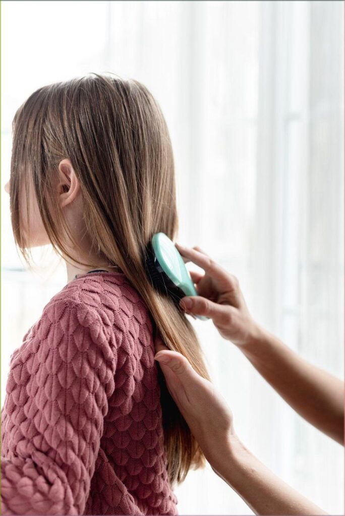 Straight, fine hair being brushed smooth with a paddle-style brush.