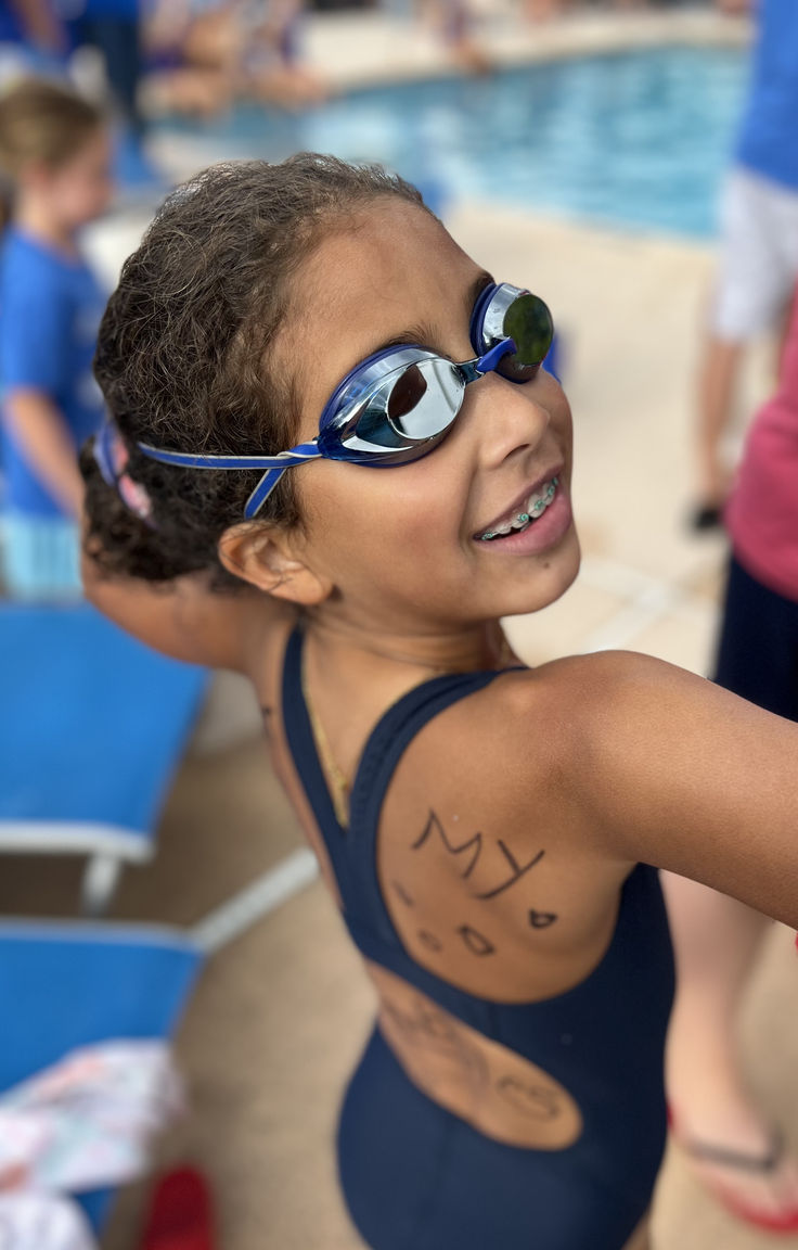Child at a swimming pool with wet hair and goggles, highlighting the importance of washing kids' hair after swimming.
