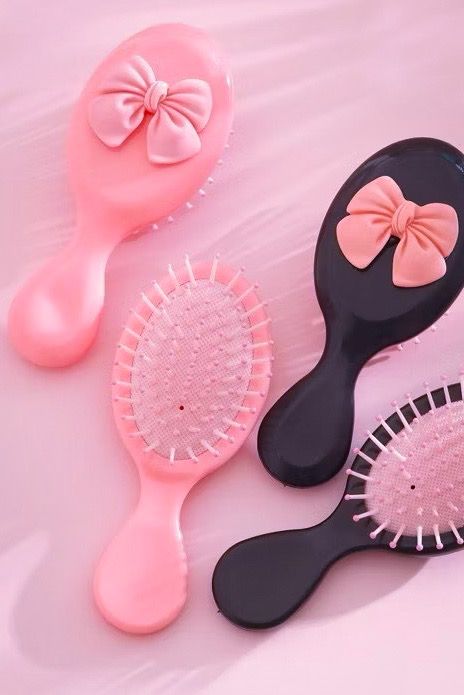 Pink and black cushion hairbrushes for kids, each topped with a matching bow, laid on a soft pink background.