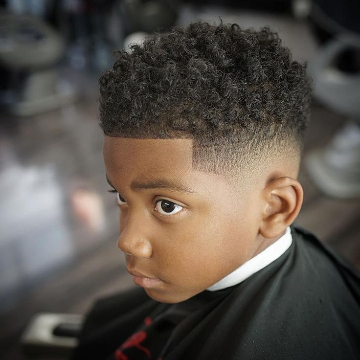 Young boy with tight curls left long on top and a fade blending down toward the ear with a sharp line up.