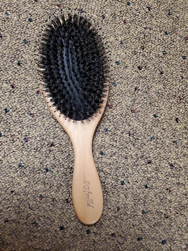 A wooden paddle brush with widely spaced pins, shown on a neutral wooden background.