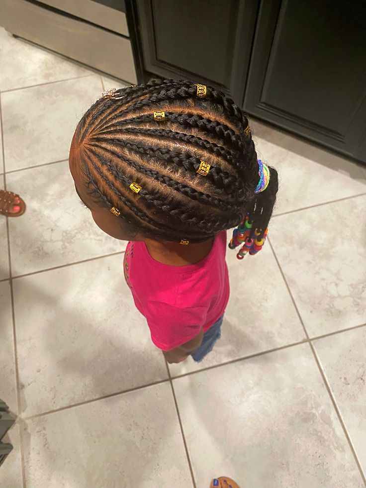 A young child wears cornrow braids decorated with small gold cuffs along each section.