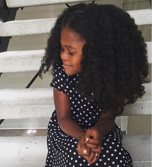 Young girl with full, defined coily hair showing healthy volume and curl definition from a consistent hair care routine.