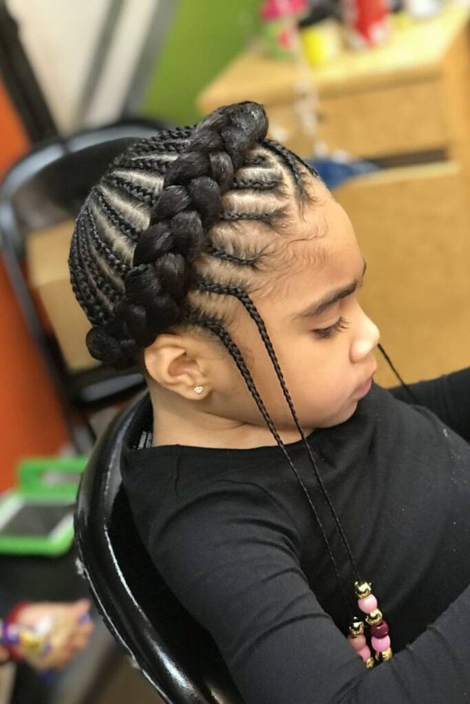 A child wears a braided crown updo with a thick braid wrapping across the top, finished with beaded strands.