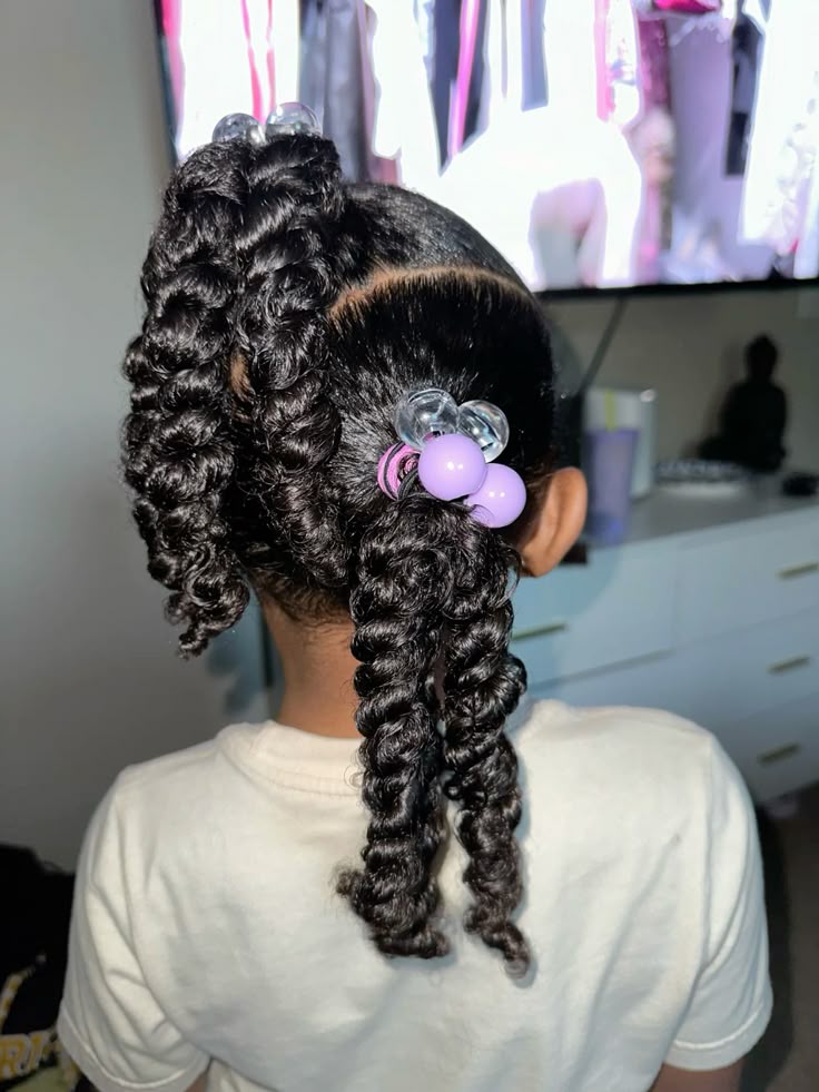 Young girl with curly hair styled in two twisted pigtails finished with purple and clear beads
