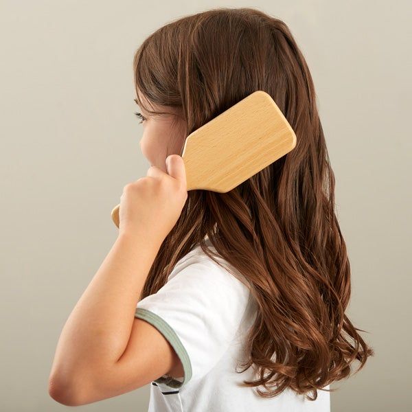 A young little girl brushing her hair with a detangling brush