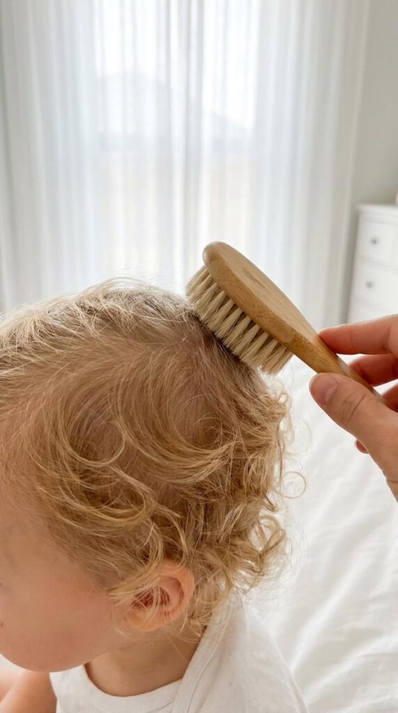 A soft bamboo brush being used to gently smooth a toddler's curly hair.
