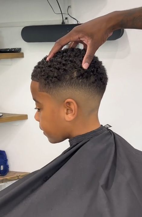 Boy getting a mid fade haircut with curly top, barber's hand shown parting the hair during the cut.