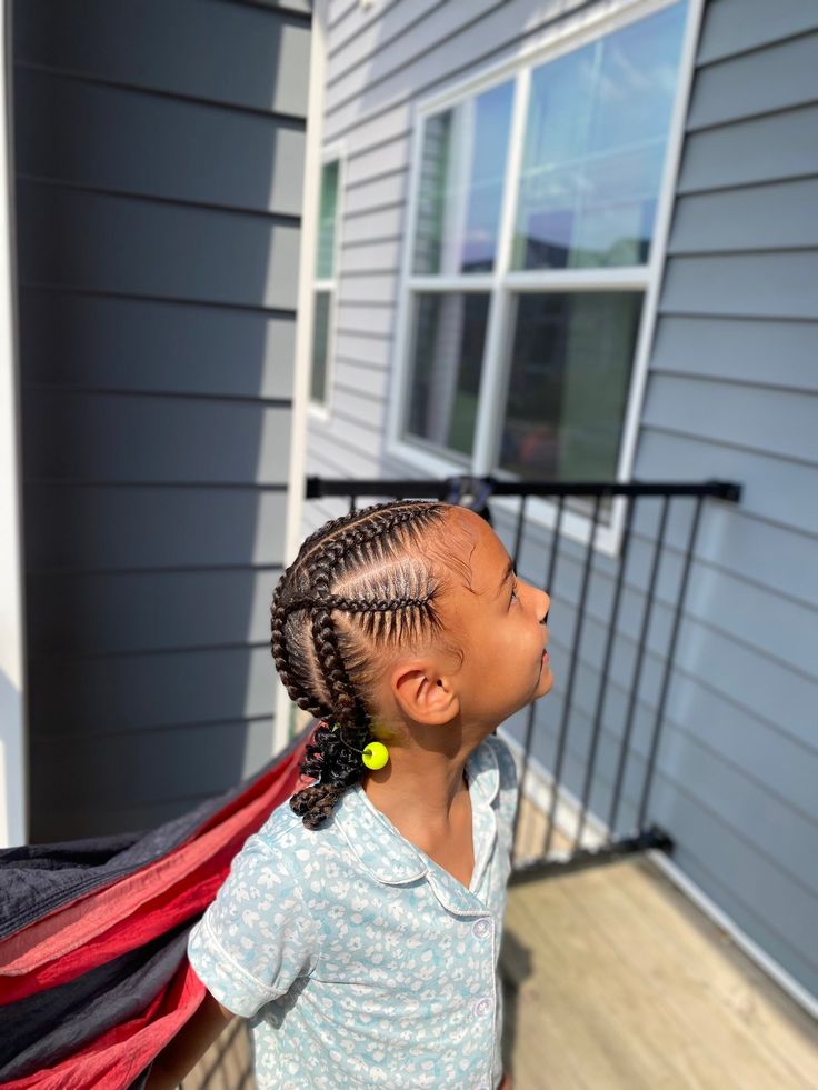 A child wears criss-cross cornrows in a diamond pattern, finished with a colorful bead at the end.