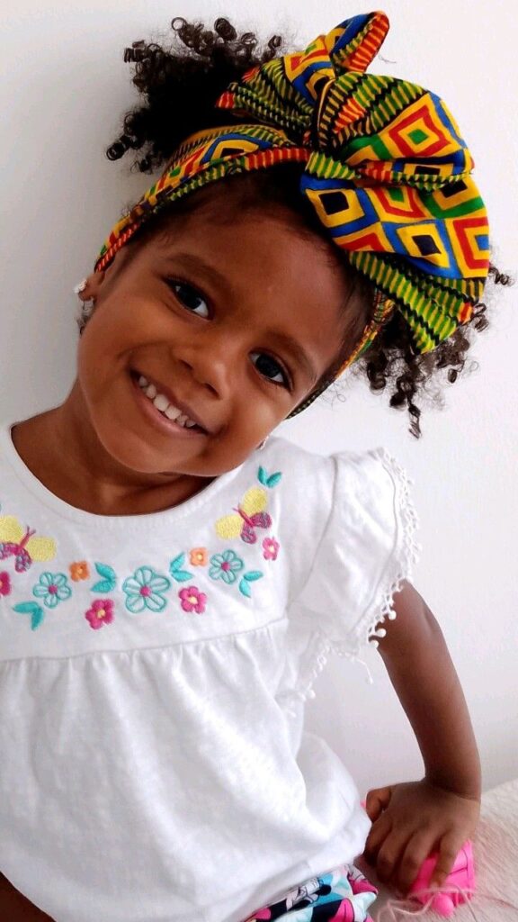 Young girl with coily hair styled in a puff wrapped with a scarf