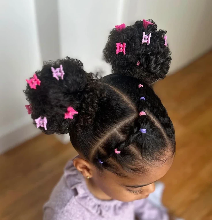 Little girl with two curly puffs and rubber band ponytail sections in pink and purple.