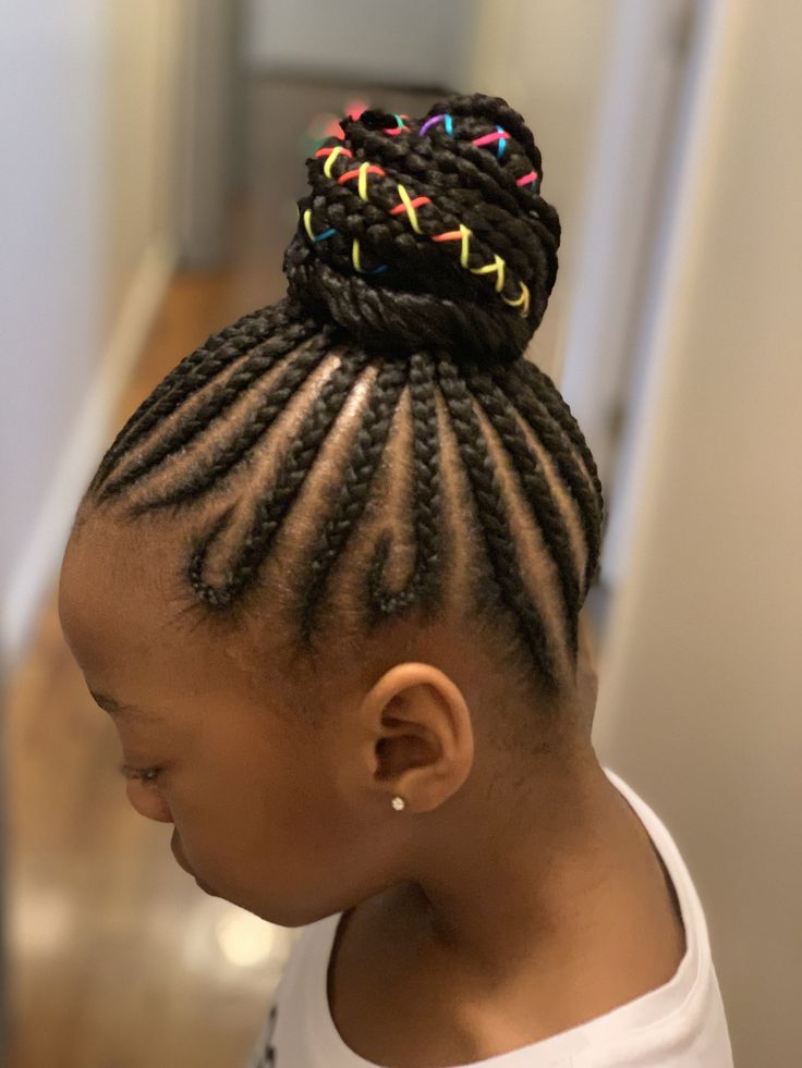  A child wears cornrows gathered into a single top knot bun, wrapped with colorful thread.