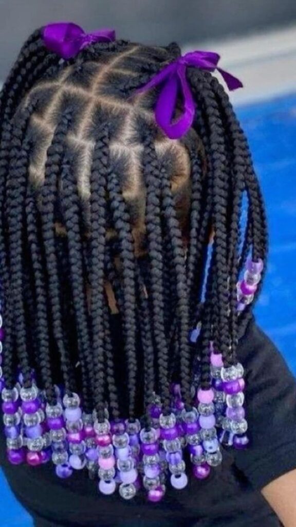 Box braid styled into cute double ponytails with purple ribbon bows ready for a special event
