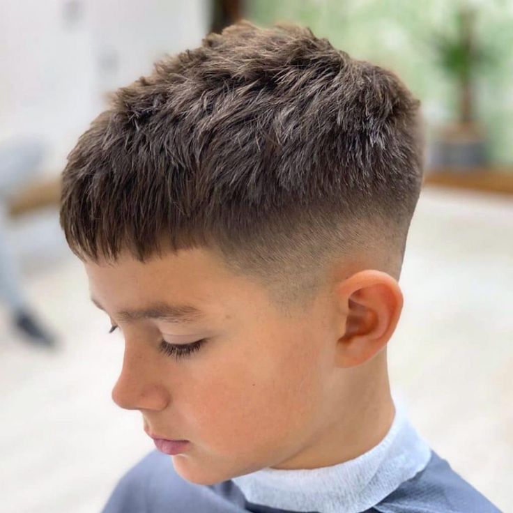 Boy with a Caesar cut hairstyle, short choppy textured top and low fade blending into the sides.