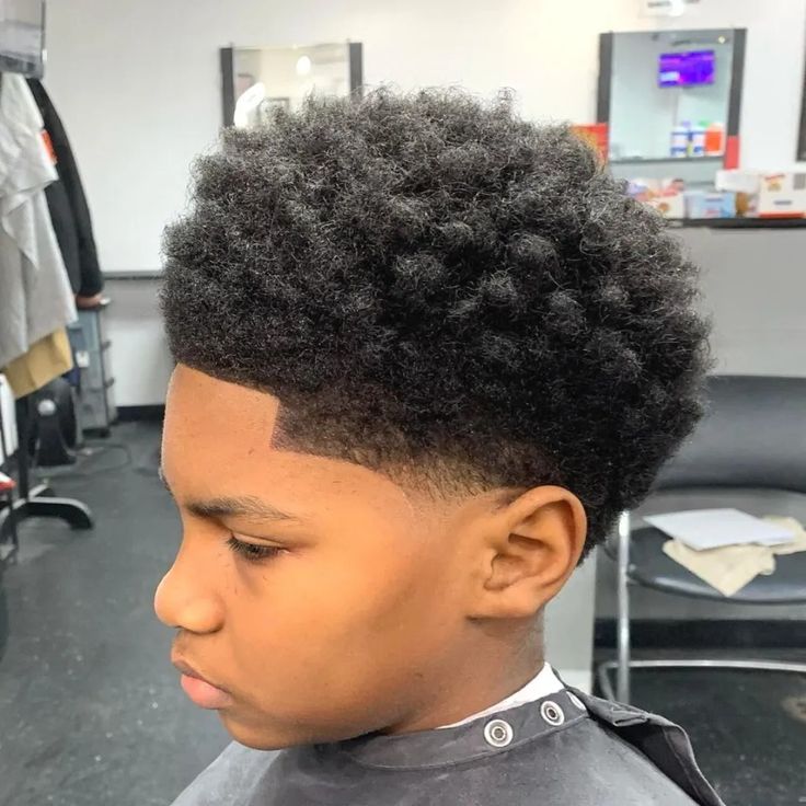 Boy with coily hair in a natural rounded shape on top and a fade blending down to a crisp line up at the front.