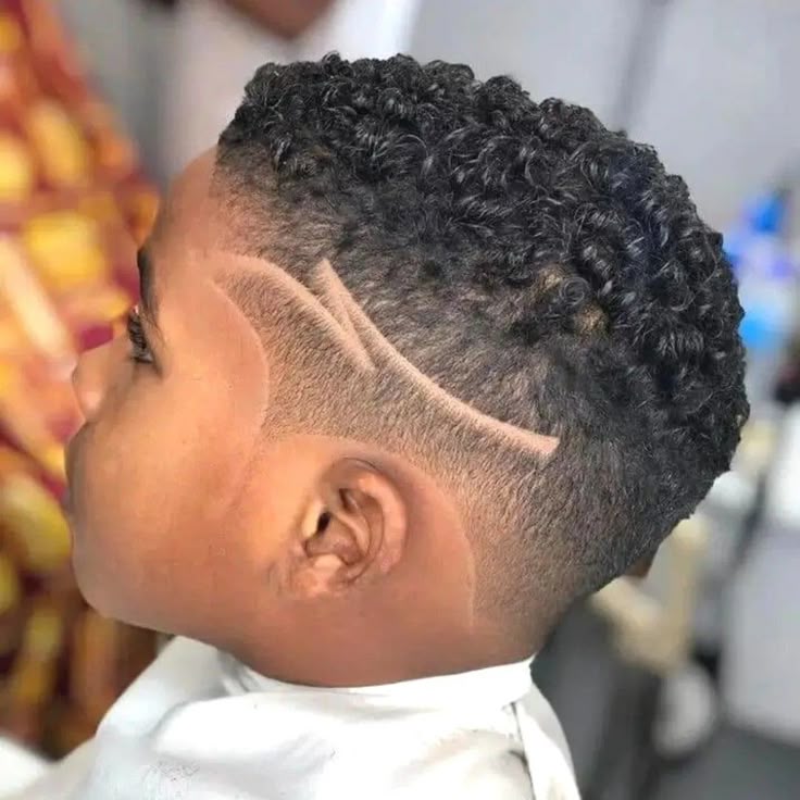 Boy with a taper fade haircut featuring a shaved-in line design above the temple and coily hair on top.