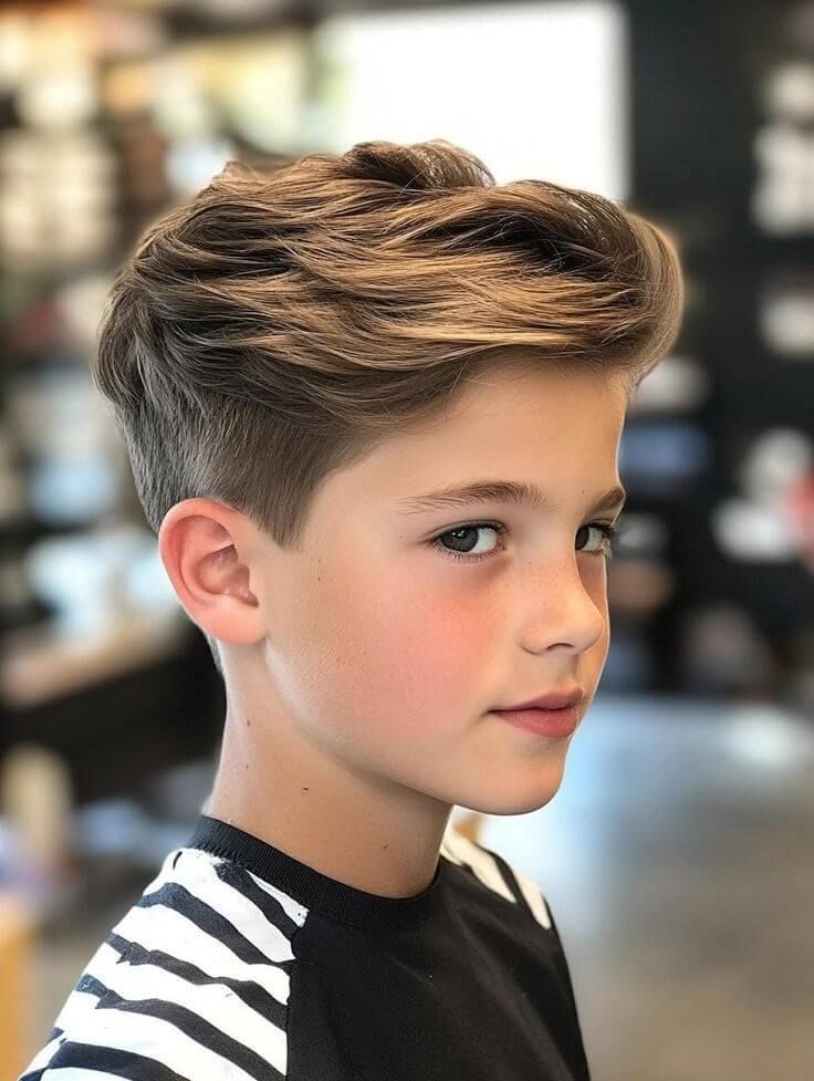 Boy with a pompadour haircut, top lifted and swept back with volume and a low fade on the sides.