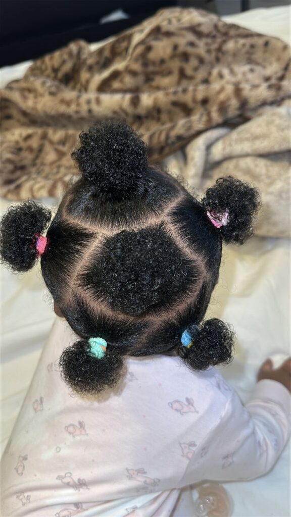 Back view of a baby's head with thick, curly hair sectioned into five puffs with colorful hair ties, showing healthy, even hair growth across the scalp."