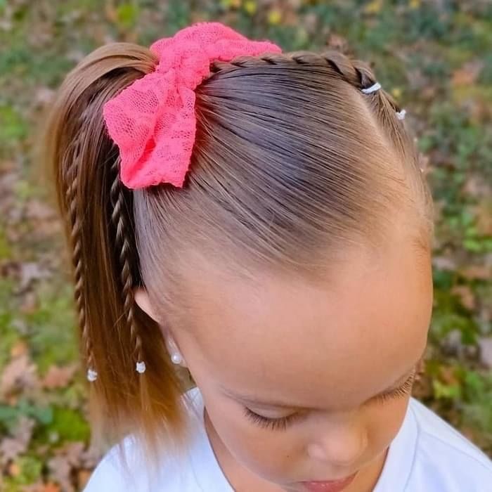 Cute  girl with a  side ponytail with braids  and a pink  bow 