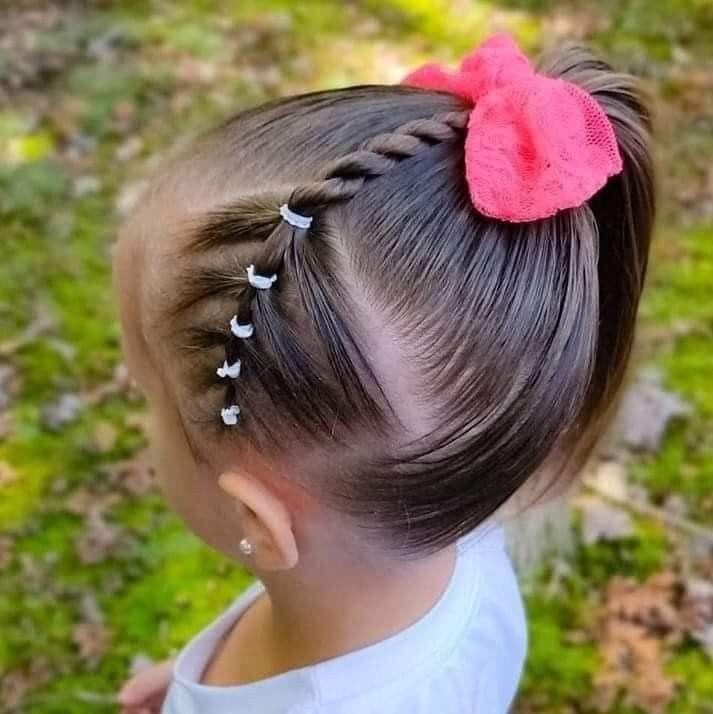 Cute little toddler with a side ponytail with a twist joined in the ponytail and a pink bow.