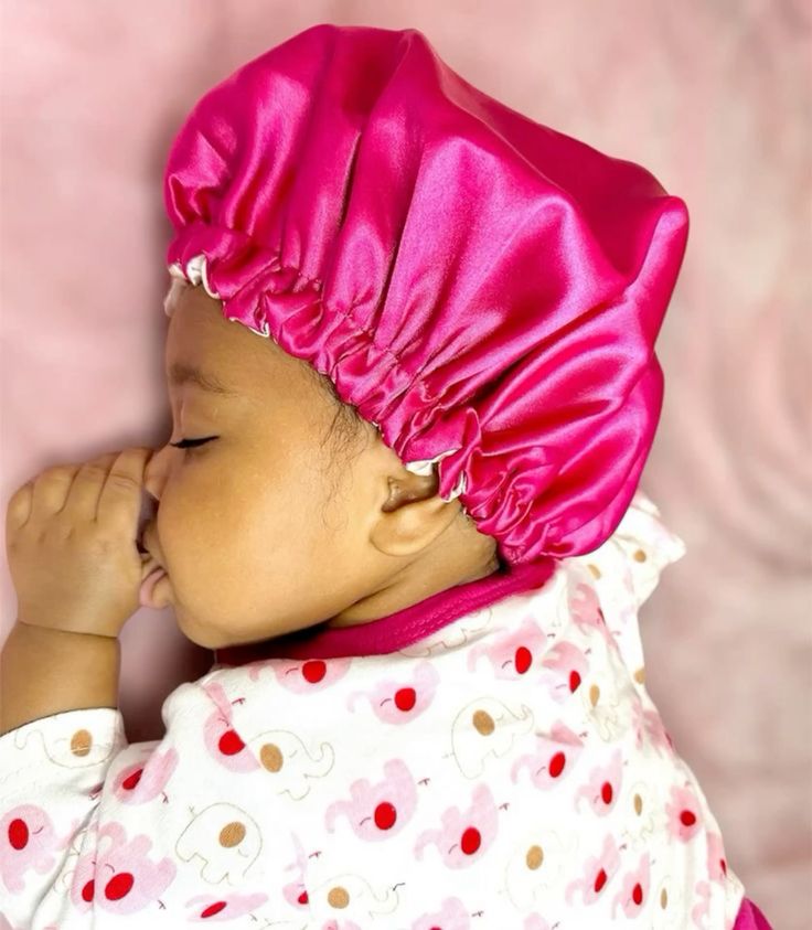 Baby sleeping in a pink satin bonnet for hair protection.