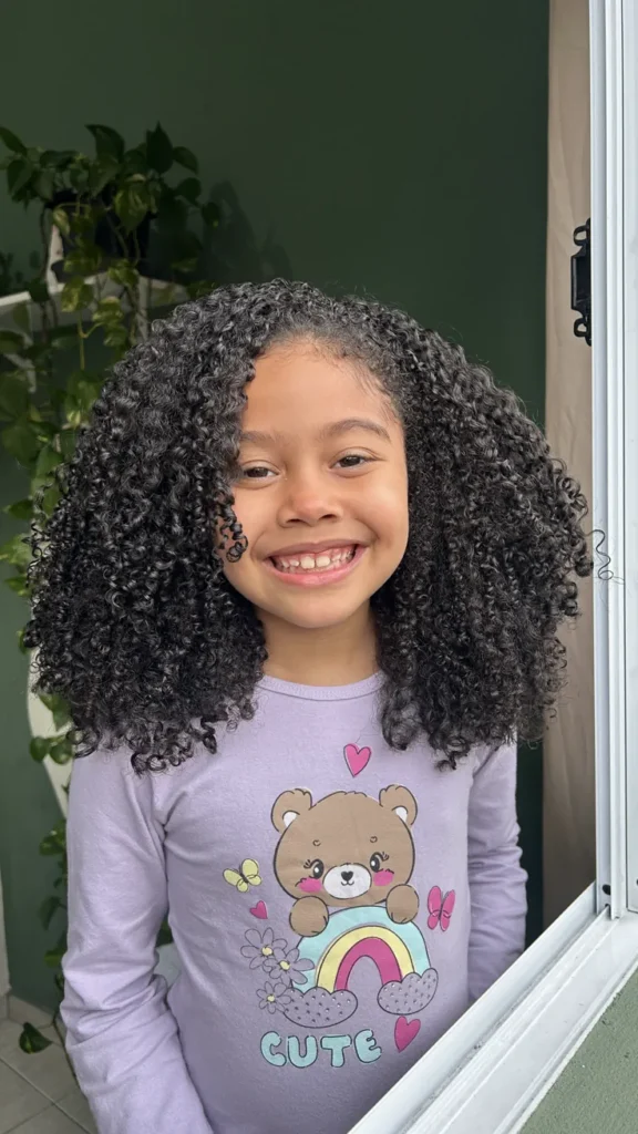 Girl with type 3 curly hair smiling near a window.