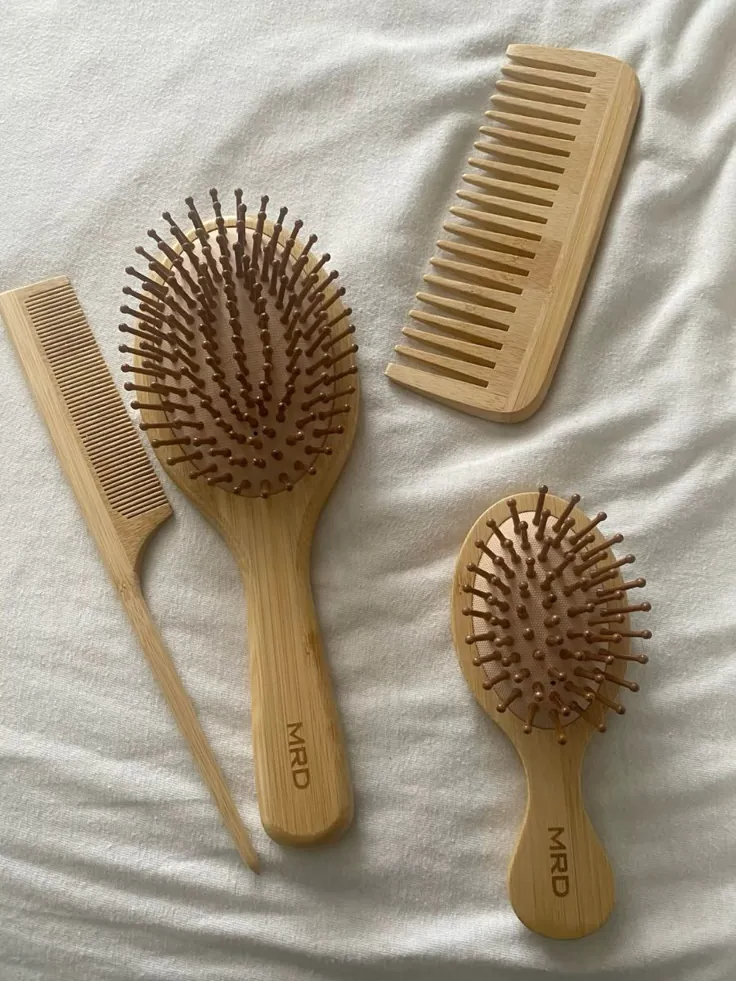A wooden detangling brush, wide-tooth comb, rattail comb, and mini brush laid out on a soft white blanket.