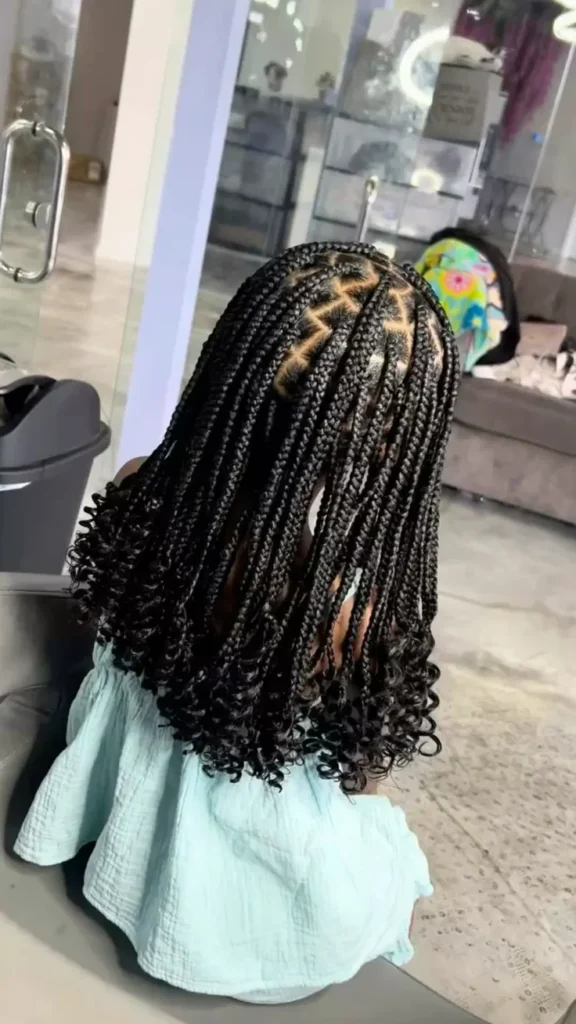 A child wears knotless braids parted into small sections, finished with curly ends cascading down her back.