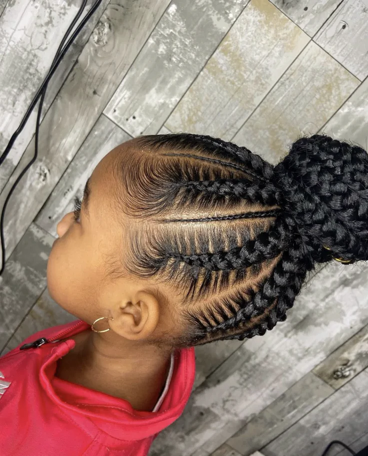 A child wears feed-in braids gathered into a full, rounded bun at the crown.