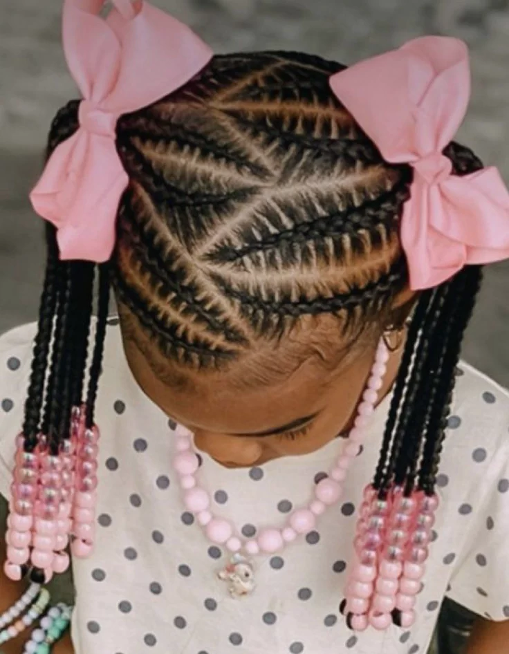 A child wears braided pigtails topped with pink bows and finished with pink beaded ends.